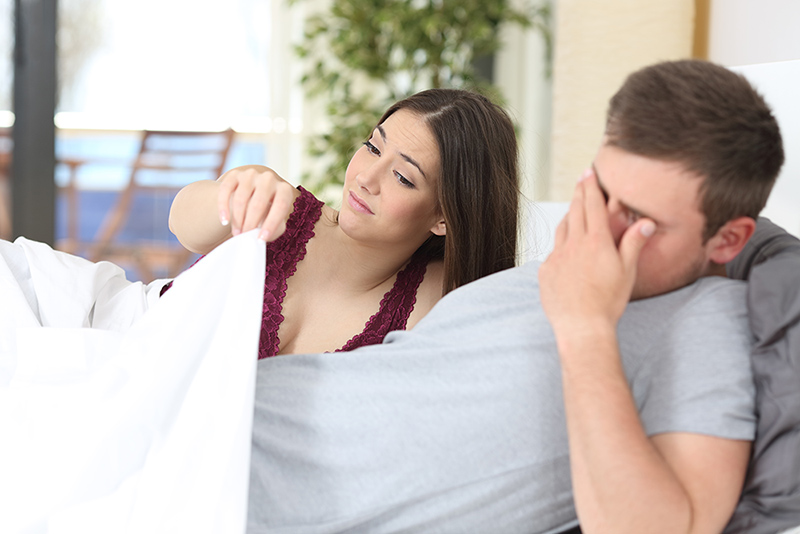 A woman peering underneath the blanket while a man covers his face in distress